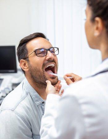 Doctor using inspection spatula to examine patient throat. ENT doctor doing throat exam. patient opened his mouth to throat check-up
