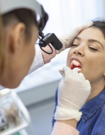 Female patient opening her mouth for the doctor to look in her throat. Otolaryngologist examines sore throat of patient.