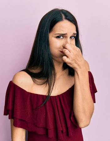 Young hispanic woman wearing casual clothes smelling something stinky and disgusting, intolerable smell, holding breath with fingers on nose. bad smell